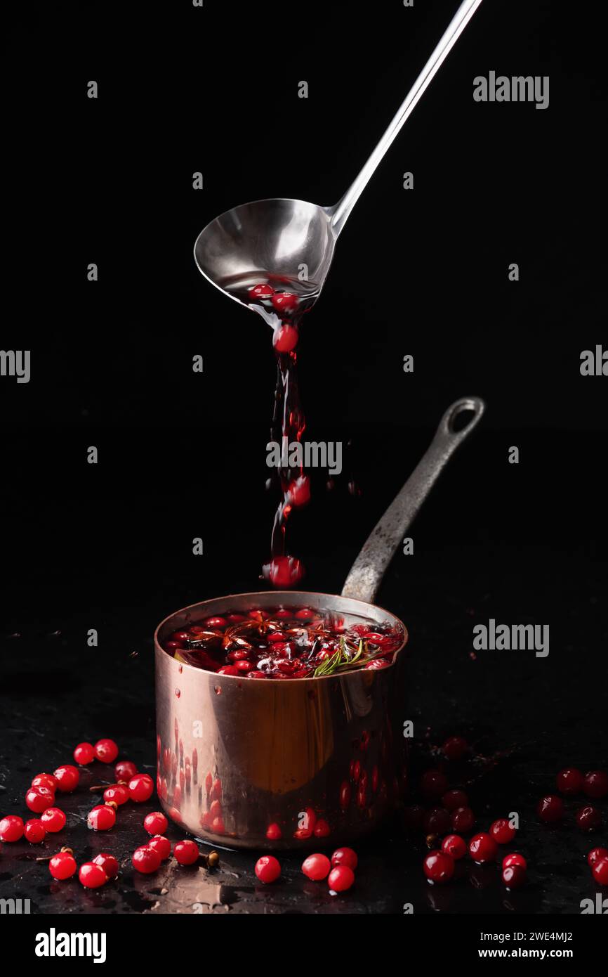 Vin chaud avec des canneberges versant dans un pot de cuivre de louche en métal sur fond noir. Photographie culinaire Banque D'Images