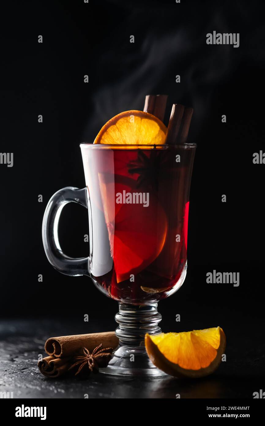 Vin chaud chaud dans un verre avec une tranche d'orange fraîche et des bâtons de cannelle sur un fond noir. Photographie de nourriture et de boissons Banque D'Images