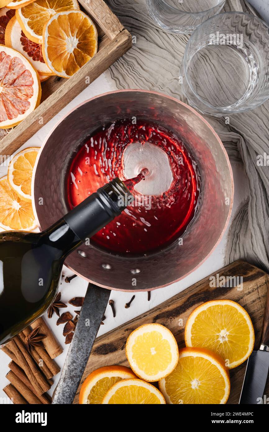 Faire du vin chaud dans la cuisine à la maison. Vin rouge versé dans un pot en cuivre. Tranches d'orange, cannelle, anis étoilé sur table. Photographie culinaire Banque D'Images