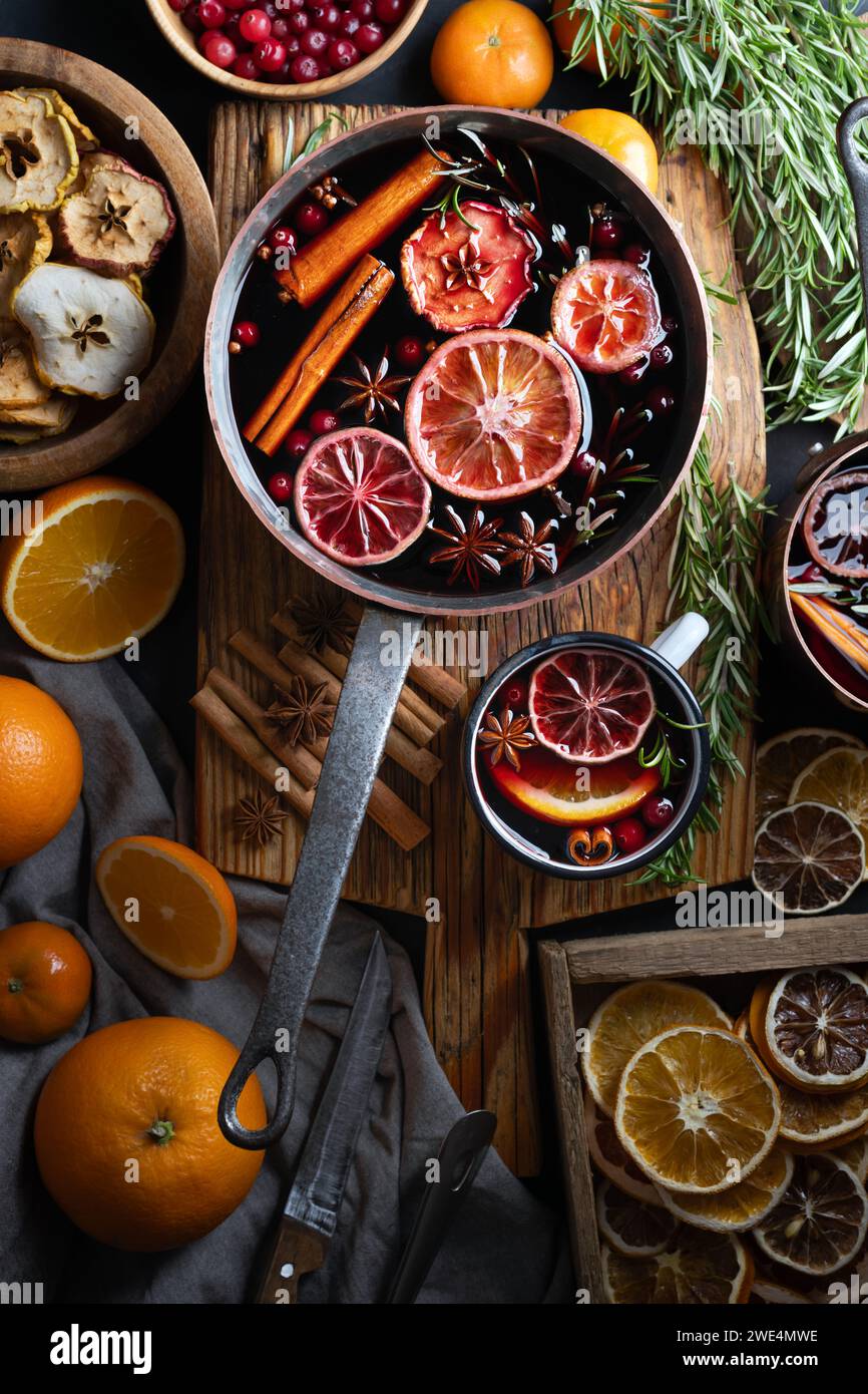 Pot en cuivre de vin chaud avec des tranches d'orange, pomme, cannelle, anis étoilé, romarin et canneberges sur table en bois. Photographie culinaire Banque D'Images