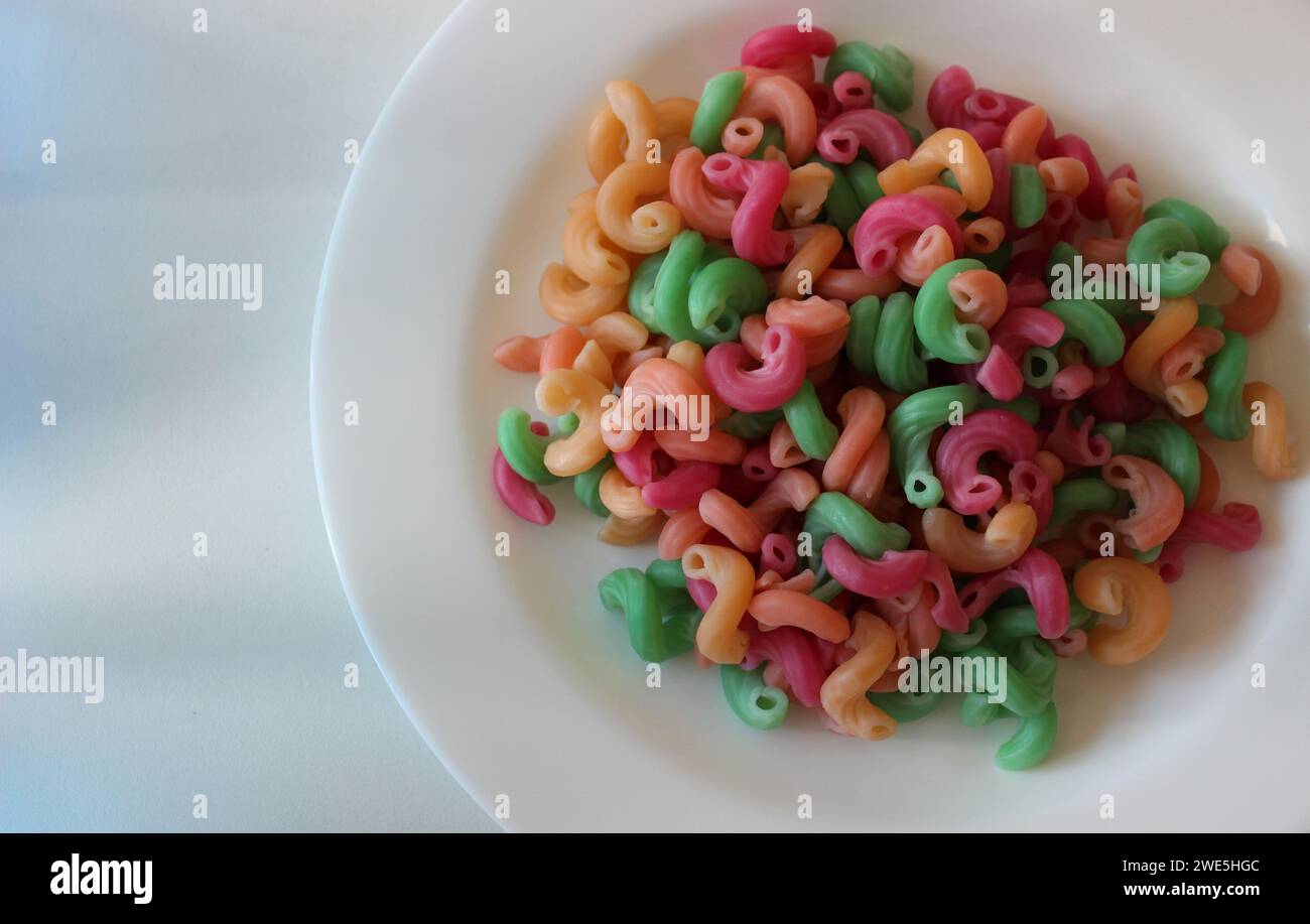 Assiette blanche avec pâtes macaroni colorées préparées isolées sur surface blanche Banque D'Images