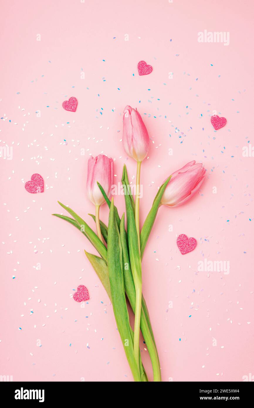 Tulipes roses et coeurs sur fond avec des confettis. Saint Valentin, concept de fête féminine. Vue de dessus, pose à plat. Banque D'Images