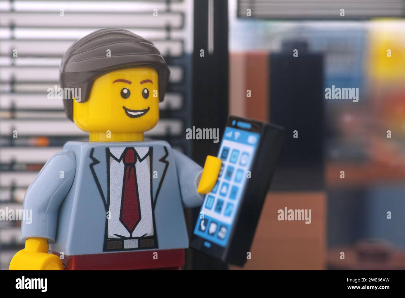 Tambov, Fédération de Russie - 23 janvier 2024 Une minifigure d'homme d'affaires Lego debout devant une fenêtre de bureau et répondant au téléphone portable. Banque D'Images
