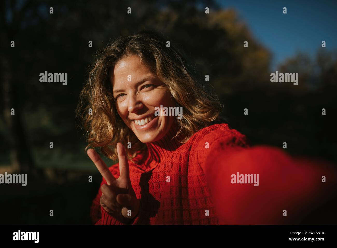 Femme souriante portant un chandail rouge et montrant signe de paix Banque D'Images