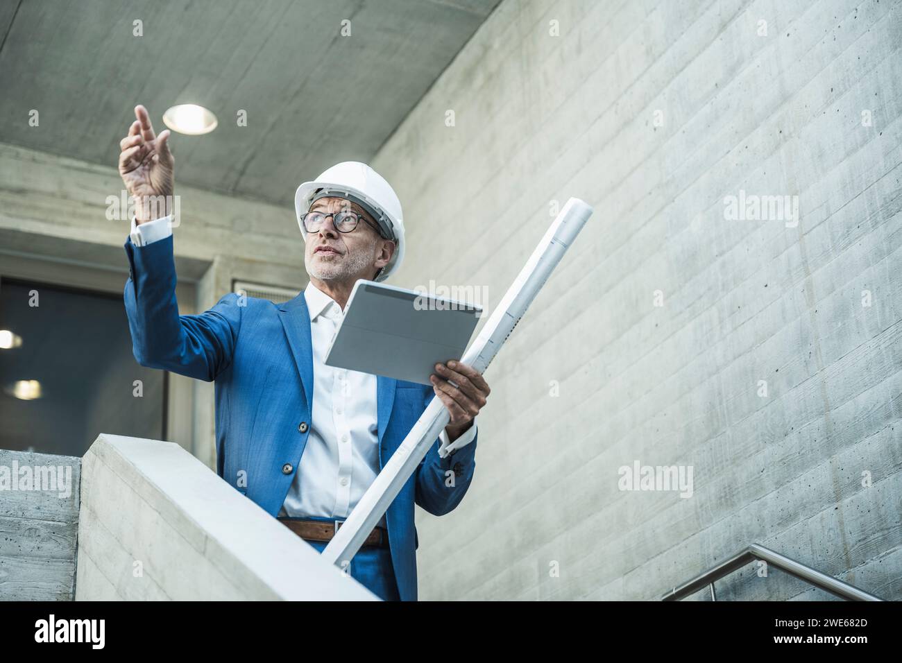 Ingénieur examinant et tenant le tablet PC avec plan près du mur Banque D'Images