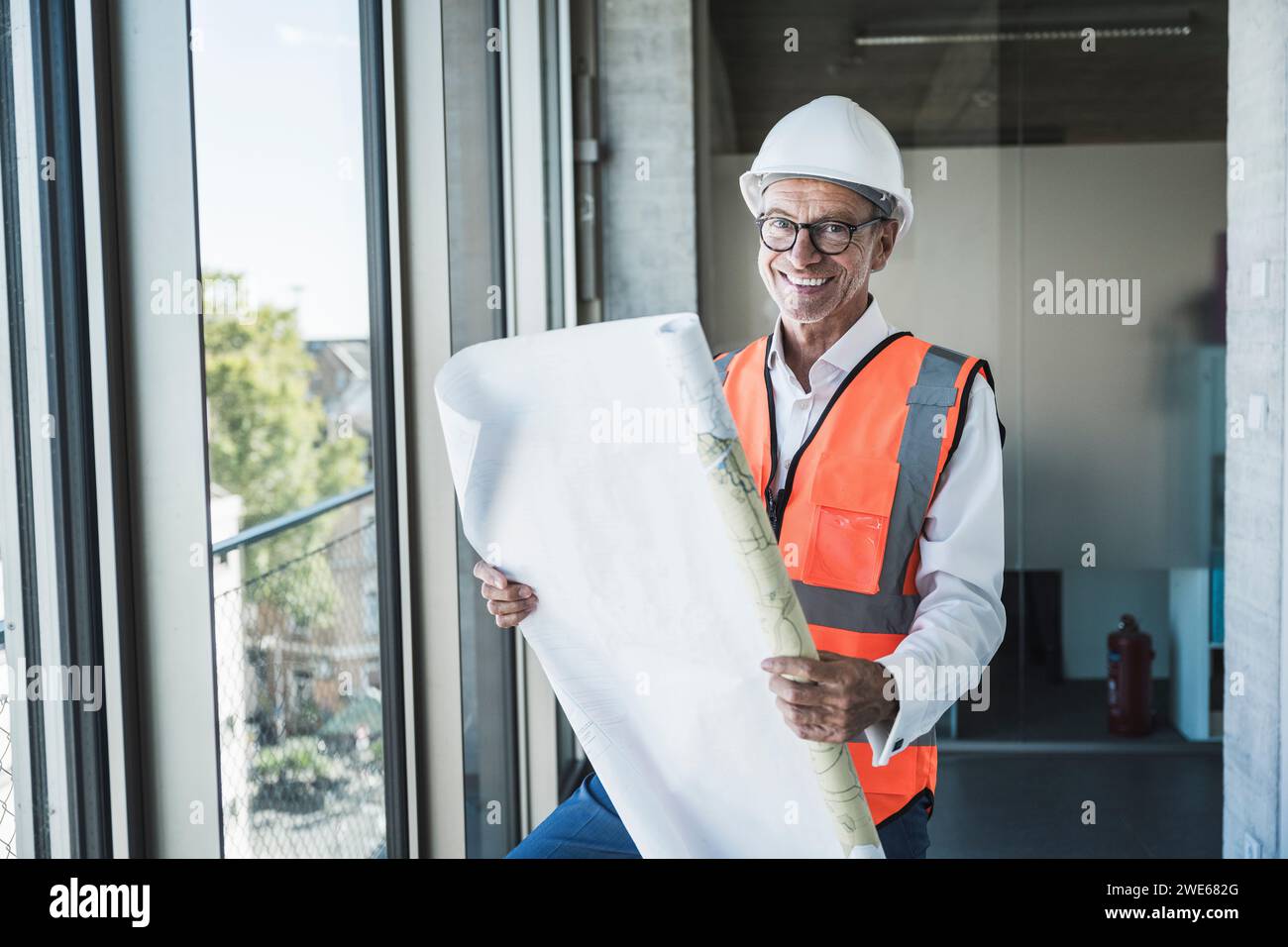 Heureux ingénieur tenant le plan près de la fenêtre dans le bureau Banque D'Images