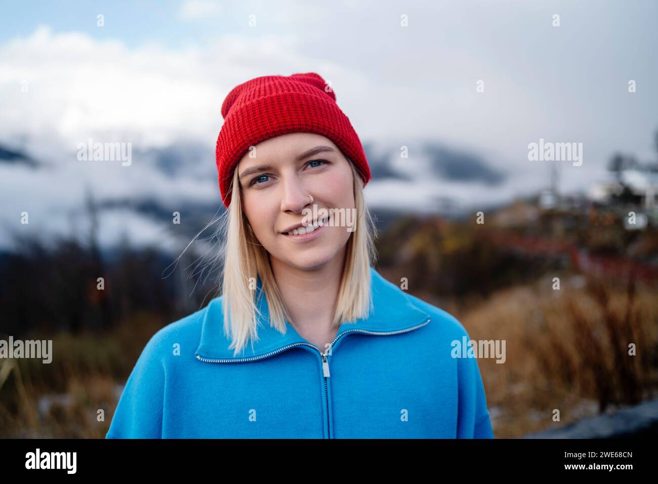 Femme souriante portant un chapeau en tricot rouge et debout sous le ciel en hiver Banque D'Images