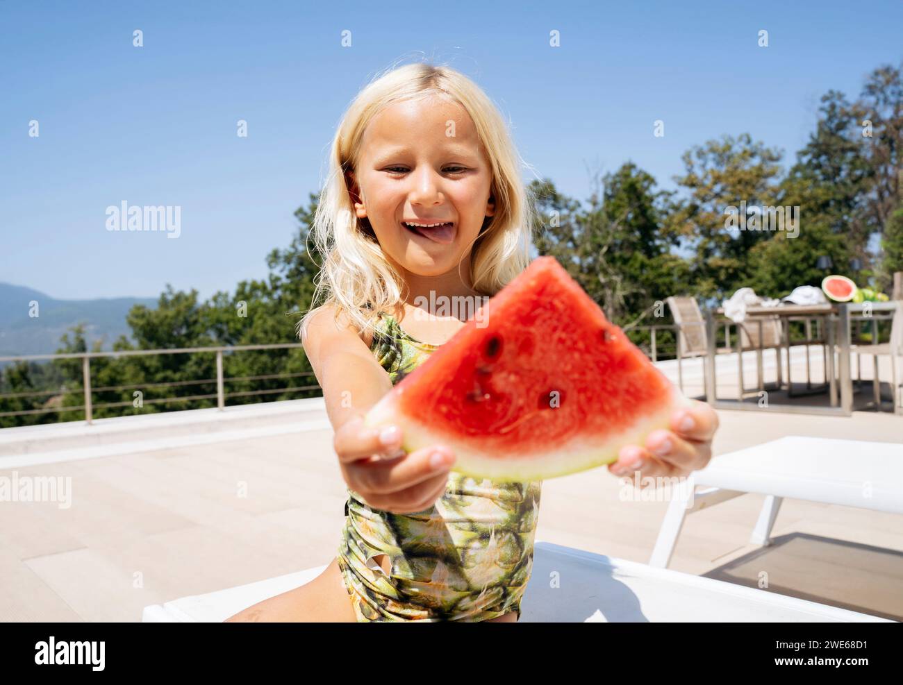 Fille souriante assise et tenant une tranche de pastèque sur une chaise longue Banque D'Images