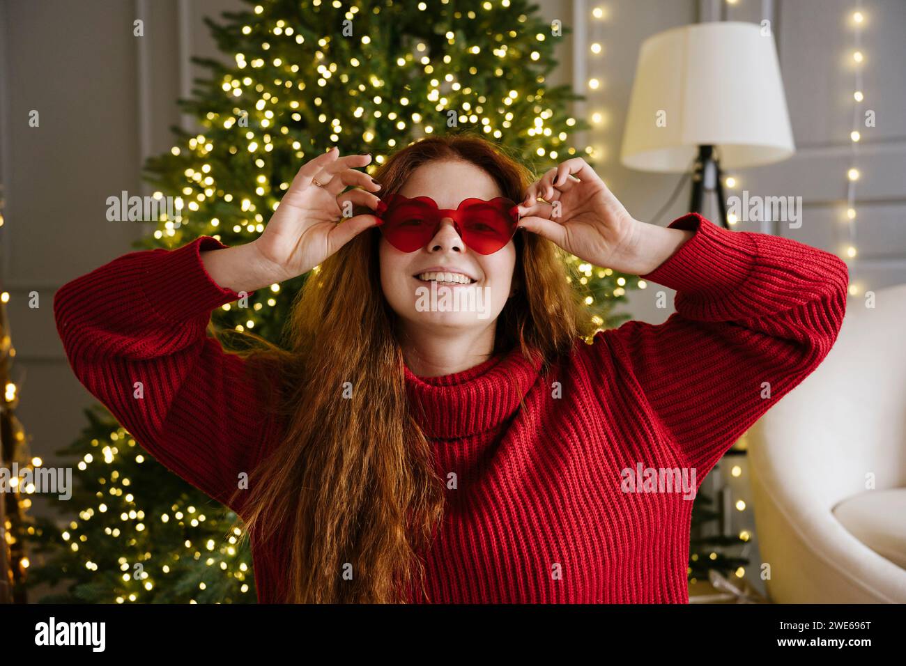 Femme souriante portant des lunettes de soleil en forme de coeur près de l'arbre de Noël à la maison Banque D'Images