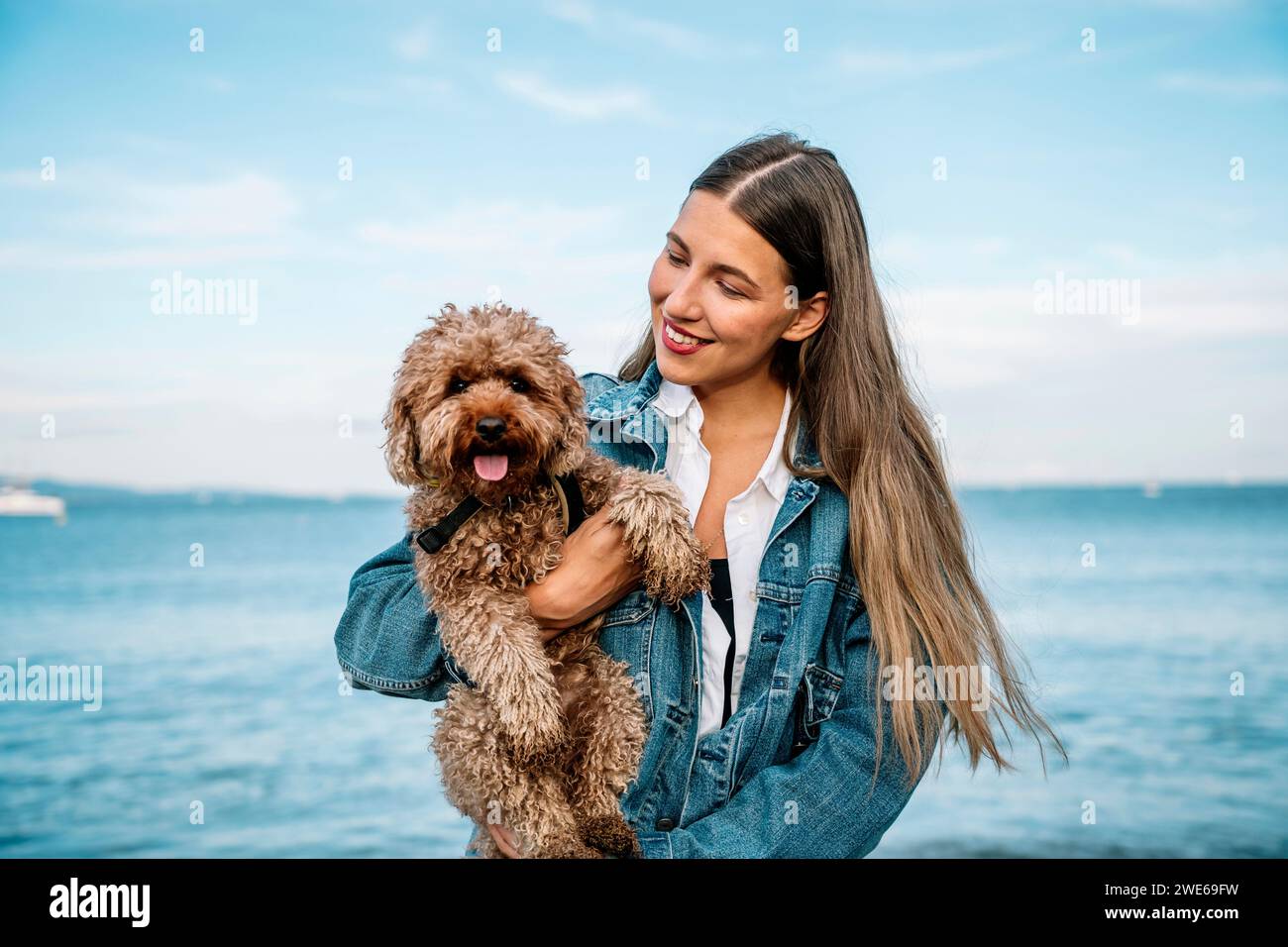 Femme souriante avec chien caniche devant la mer Banque D'Images