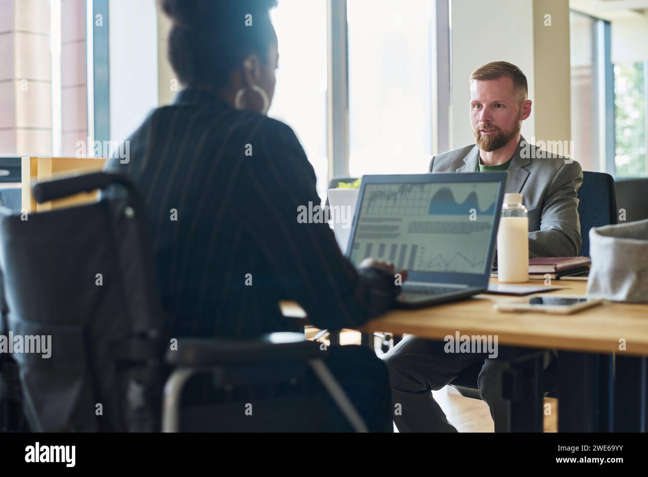 Femme d'affaires en fauteuil roulant discutant avec l'homme d'affaires sur des tableaux et des graphiques Banque D'Images