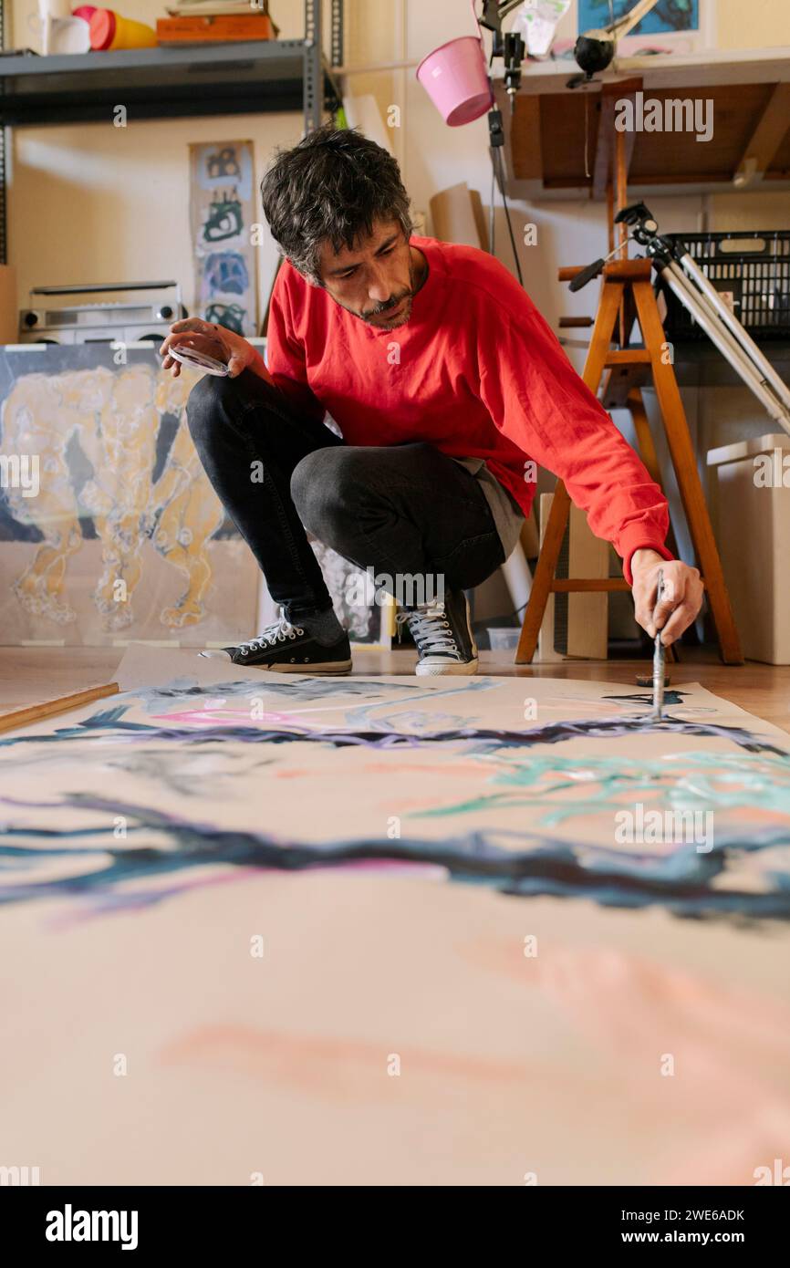 Artiste mature accroupissant et peignant sur toile à l'atelier Banque D'Images