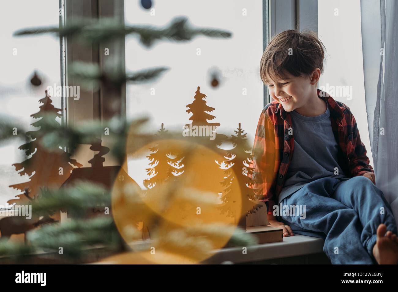 Garçon souriant admirant la décoration de Noël près de la fenêtre à la maison Banque D'Images