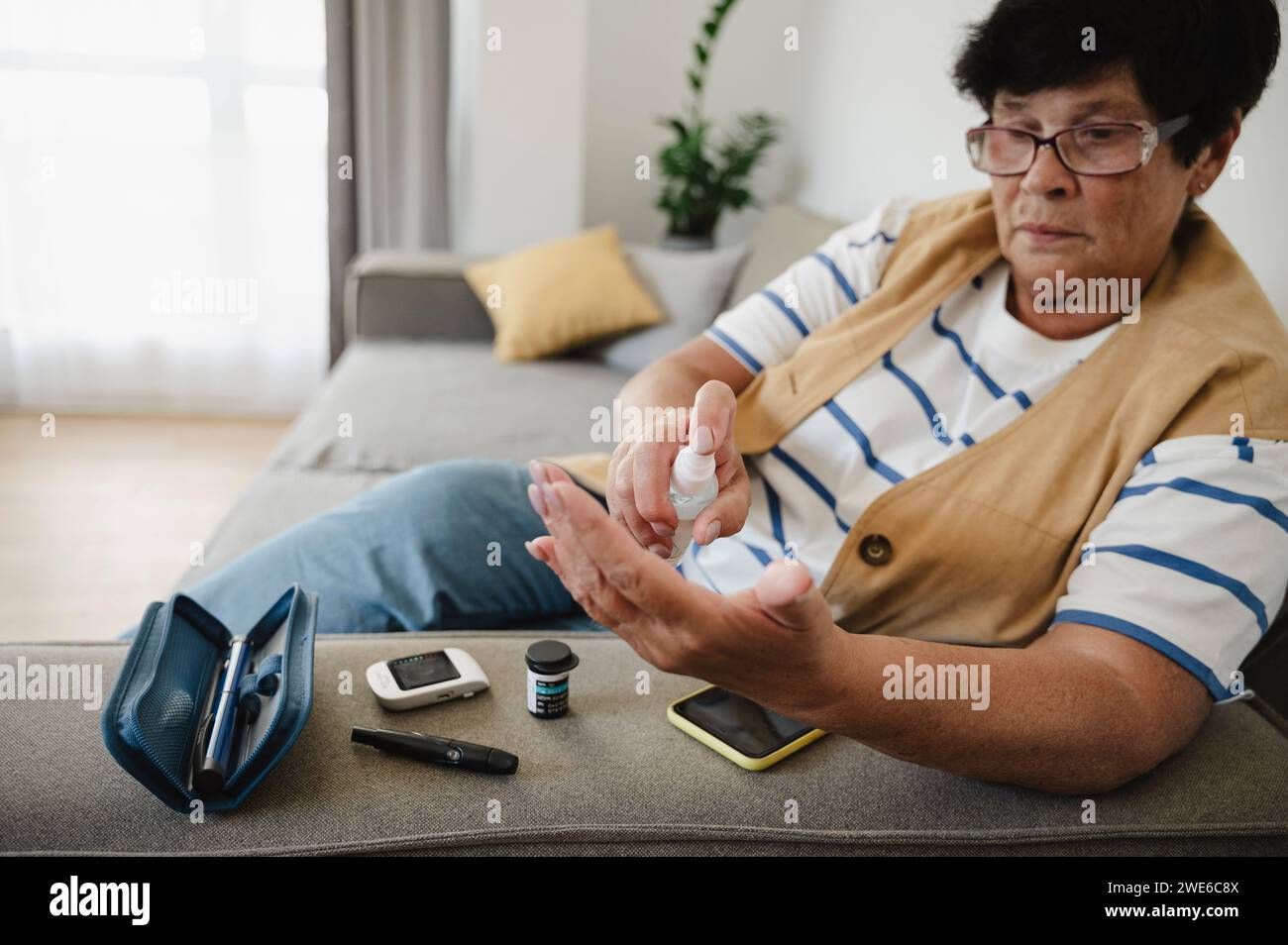 Femme âgée utilisant un désinfectant pour le test de glycémie à la maison Banque D'Images
