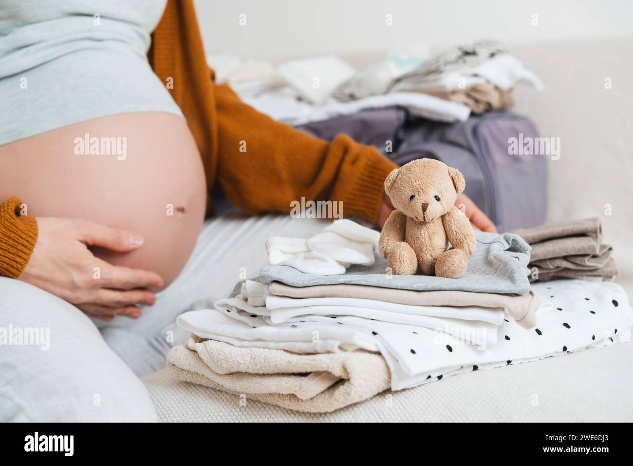 Femme enceinte assise avec un ours en peluche et emballant des vêtements à la maison Banque D'Images