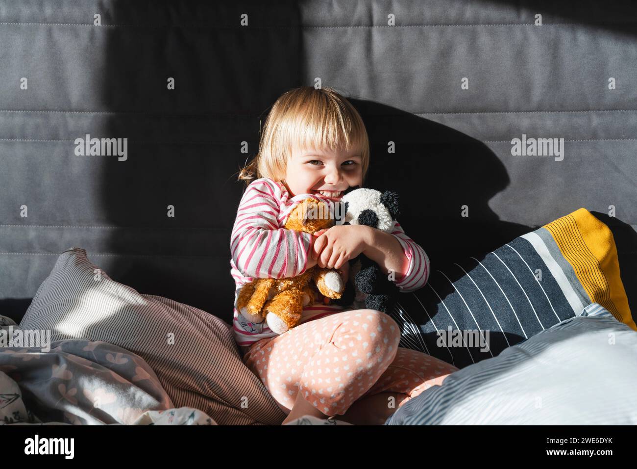 Fille joyeuse serrant des jouets en peluche sur le lit à la maison Banque D'Images