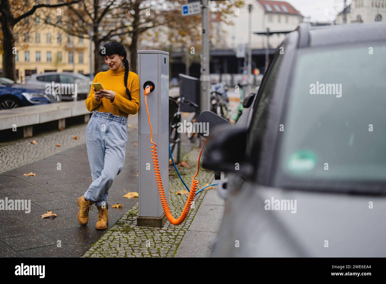 Femme utilisant un téléphone intelligent et la voiture de charge à la gare Banque D'Images