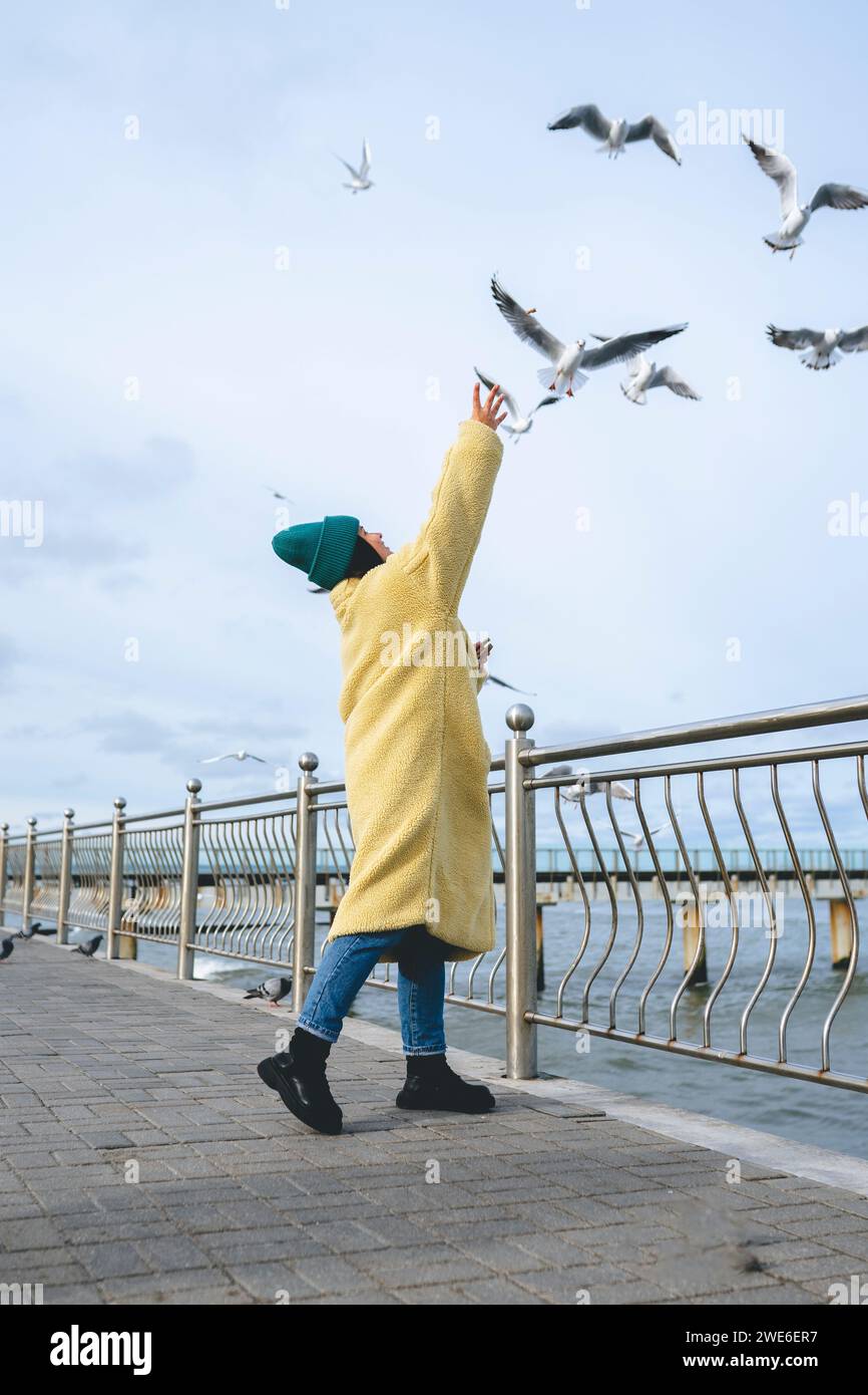 Femme debout près de la rambarde et atteignant les mouettes volant près de la mer Banque D'Images