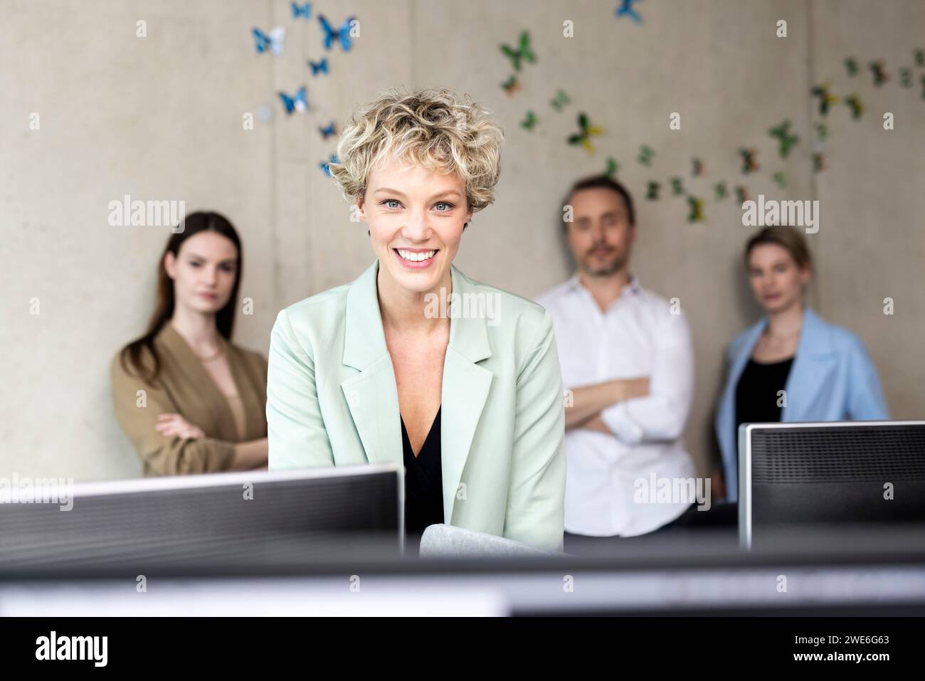 Femme d'affaires souriante avec des collègues en arrière-plan sur le lieu de travail Banque D'Images