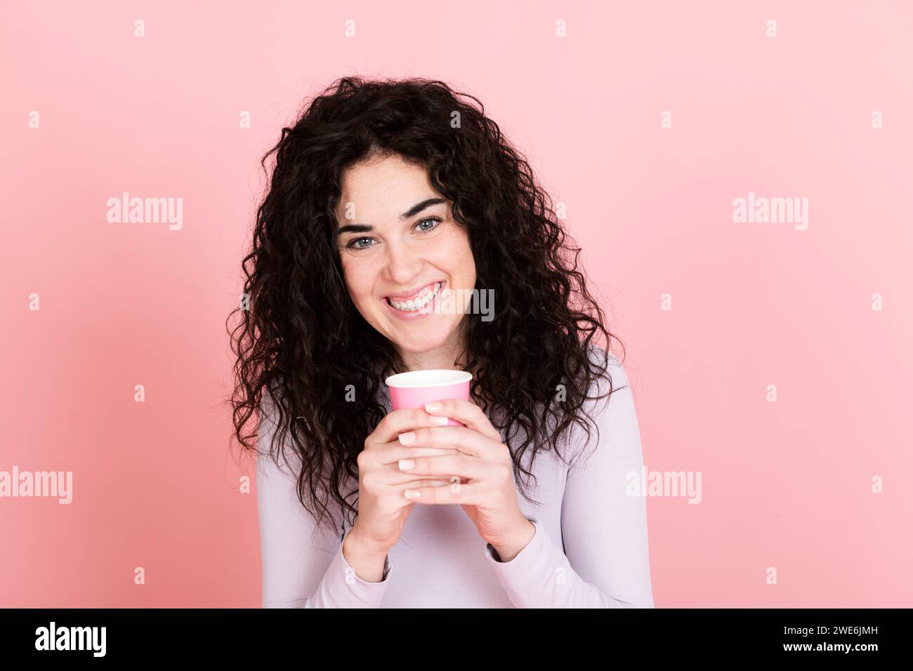 Femme heureuse tenant tasse à café jetable sur fond rose Banque D'Images