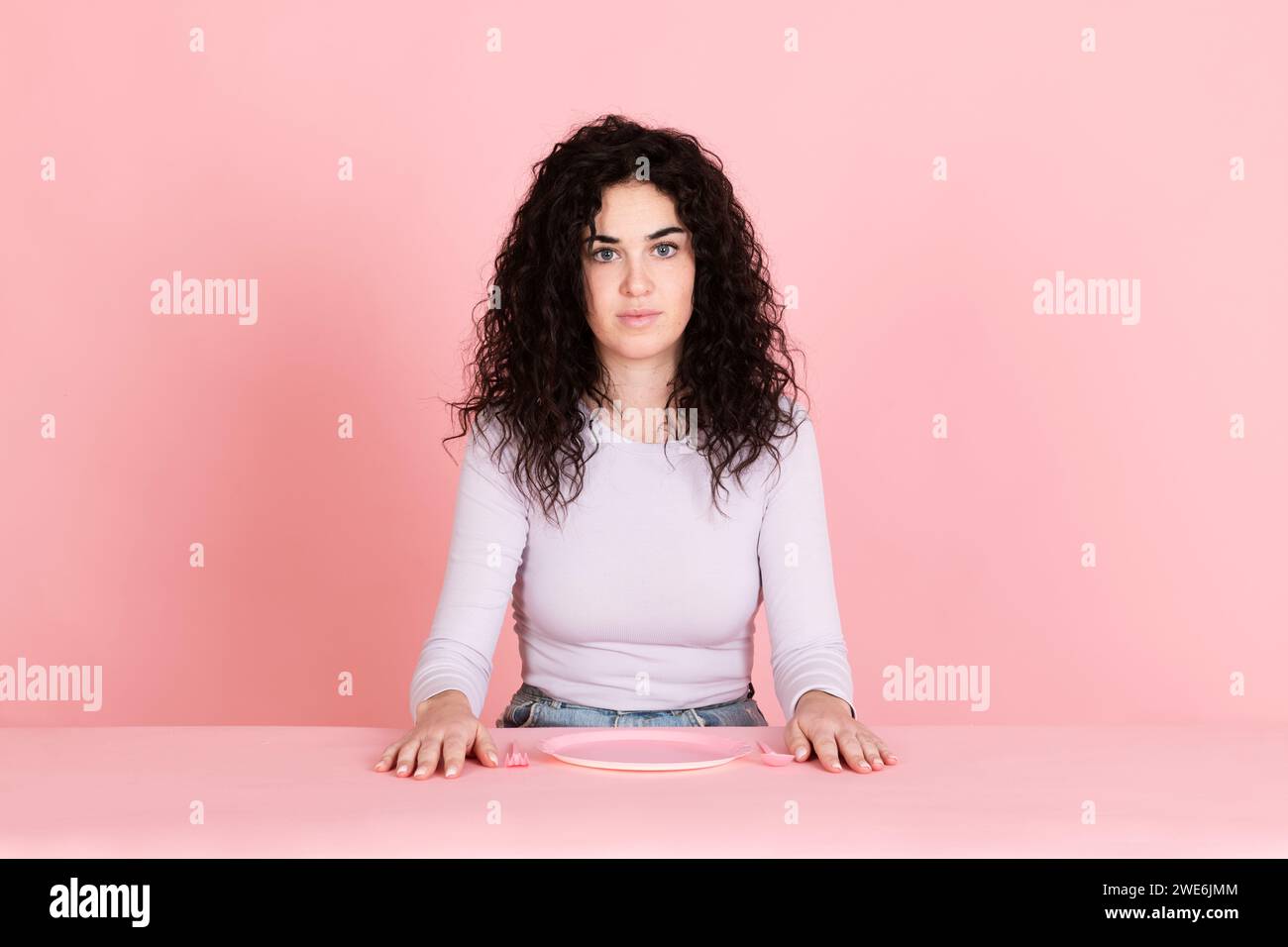 Jeune femme assise avec une assiette vide sur fond rose Banque D'Images