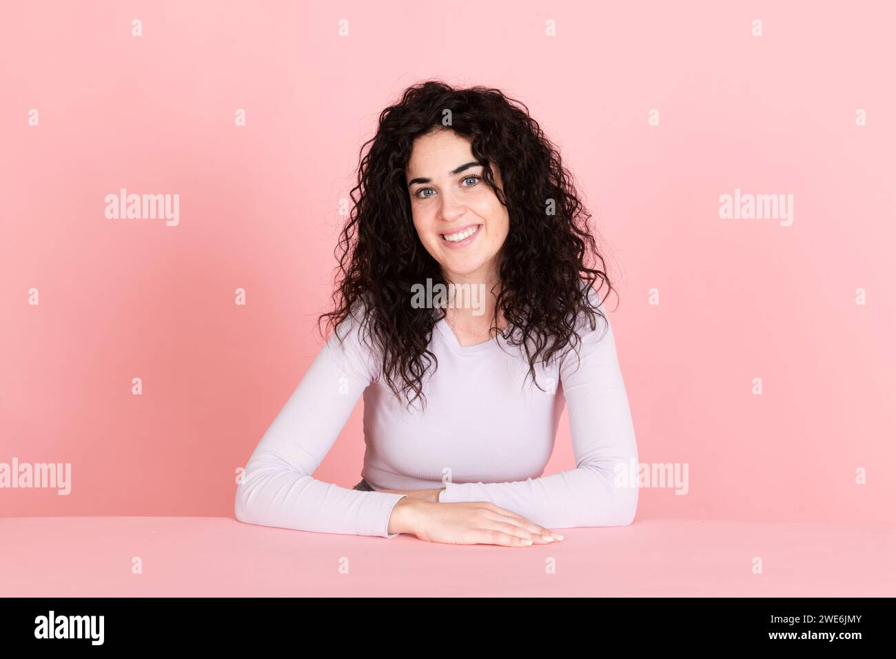 Heureuse jeune femme assise à table sur fond rose Banque D'Images