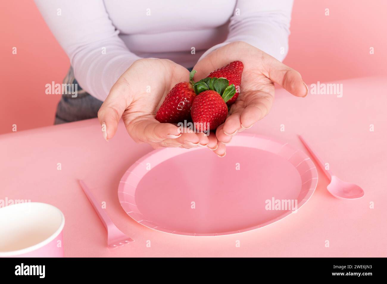 Femme tenant des fraises en main sur une assiette vide rose Banque D'Images
