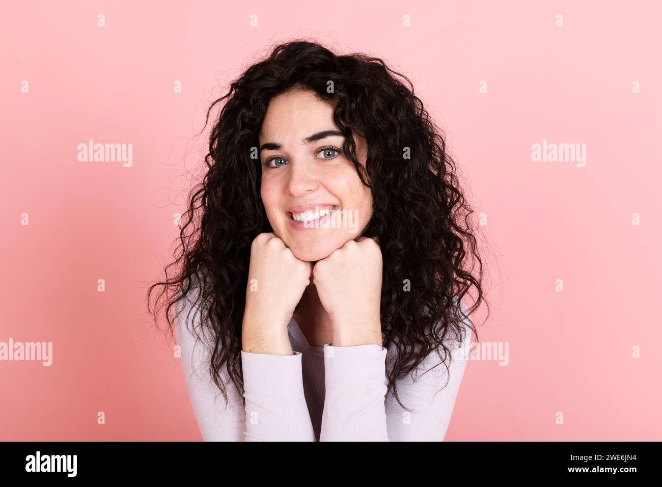 Jeune femme souriante avec les mains sur le menton sur fond rose Banque D'Images