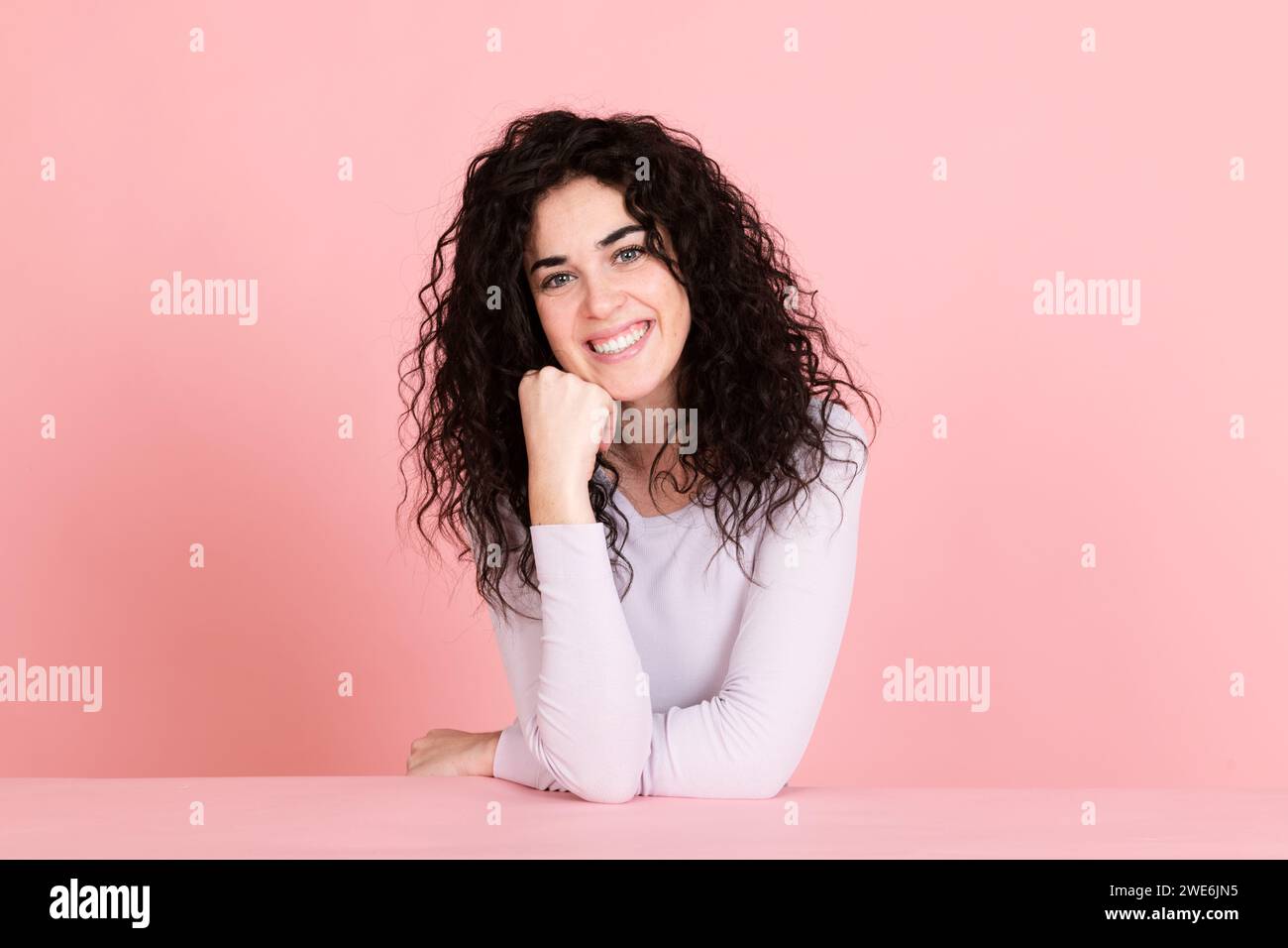 Jeune femme souriante assise à table sur fond rose Banque D'Images
