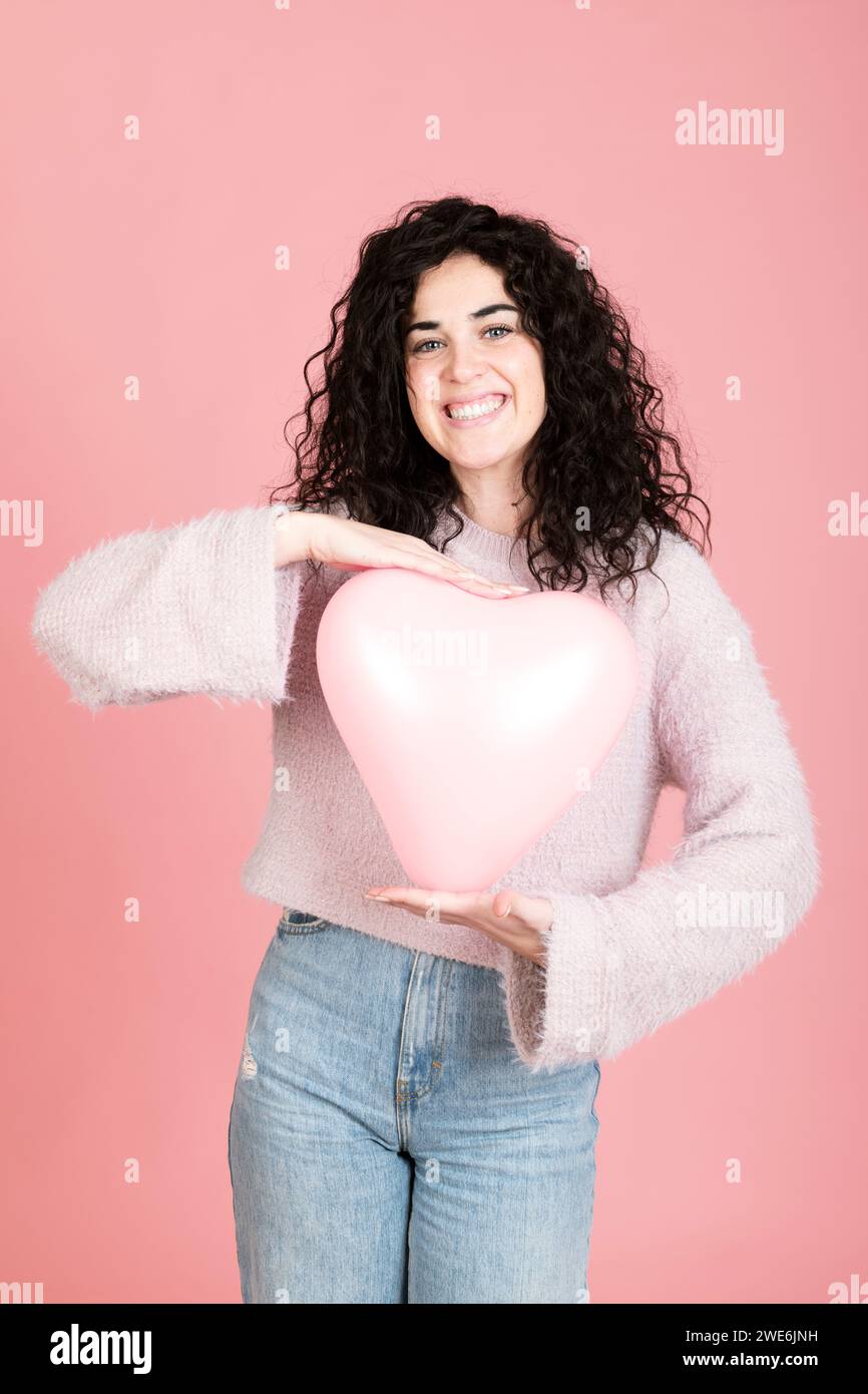 Jeune femme souriante debout avec ballon en forme de coeur sur fond rose Banque D'Images