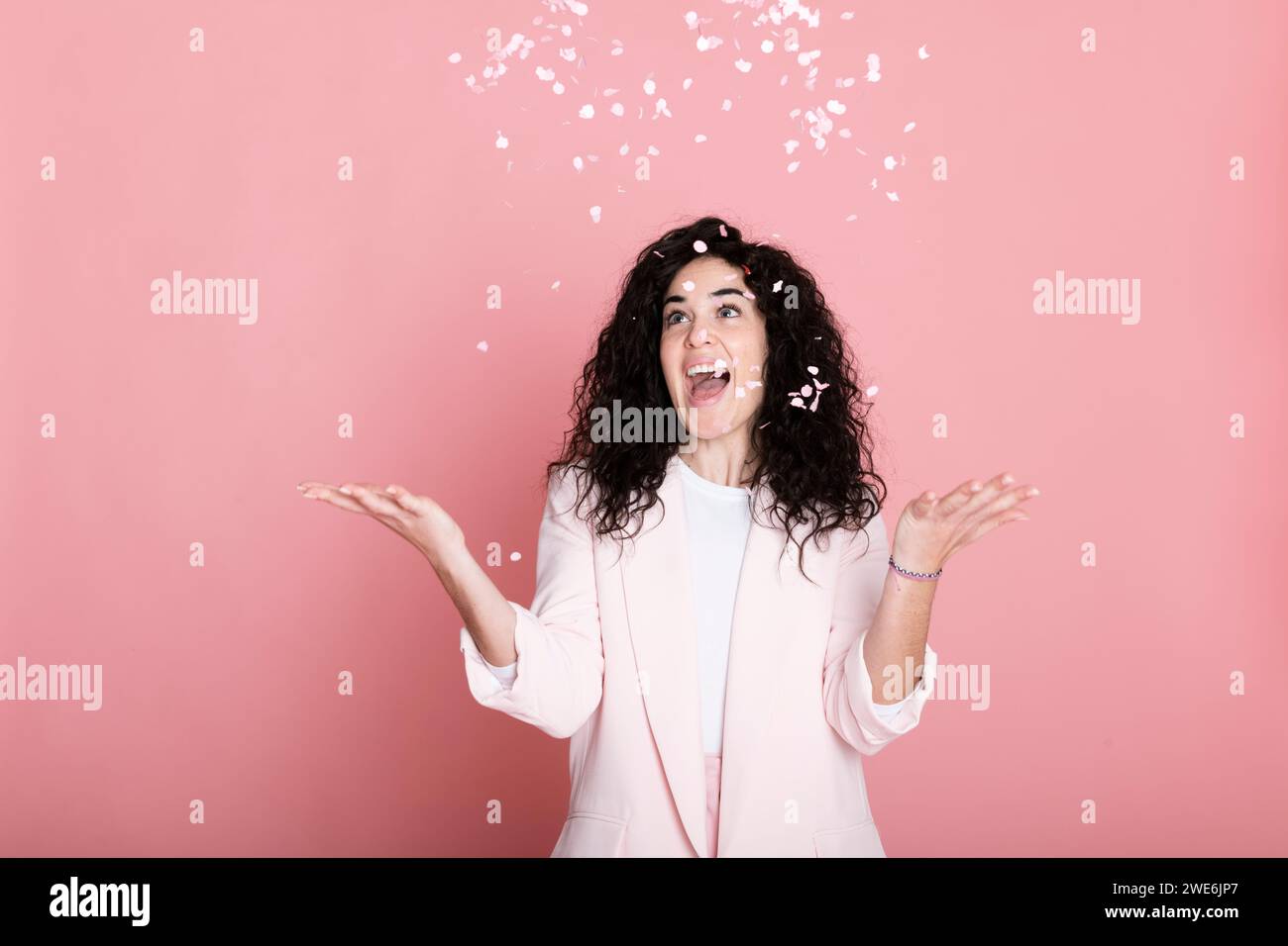 Jeune femme joyeuse attrapant des confettis sur fond rose Banque D'Images