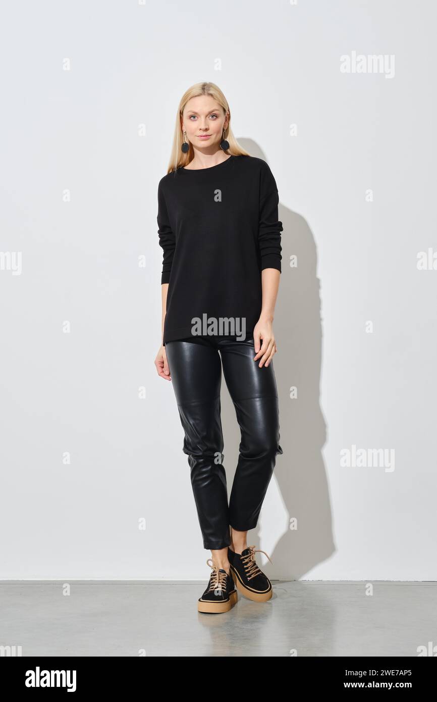 Femme tendance en pull noir et pantalon en cuir posant dans le studio lumineux Banque D'Images
