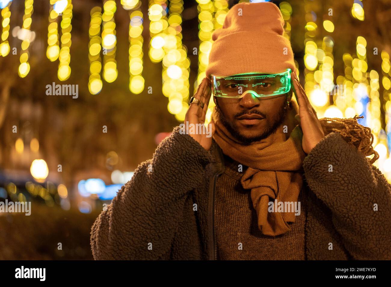 Homme africain dans des vêtements chauds utilisant des lunettes intelligentes la nuit dans la ville pendant la saison de Noël Banque D'Images