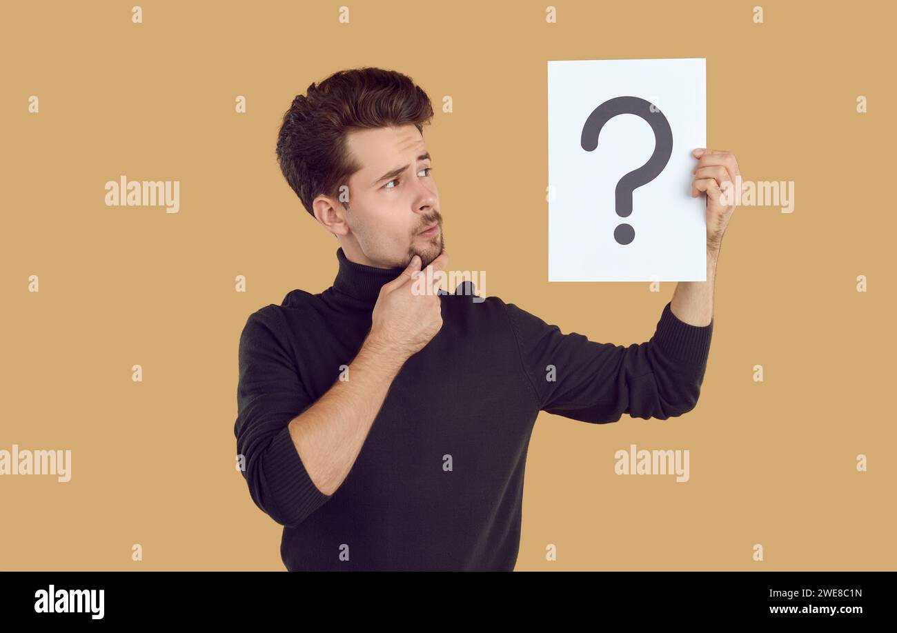 L'homme pensif regarde un morceau de papier avec un point d'interrogation dessiné dessus, qu'il tient en main Banque D'Images