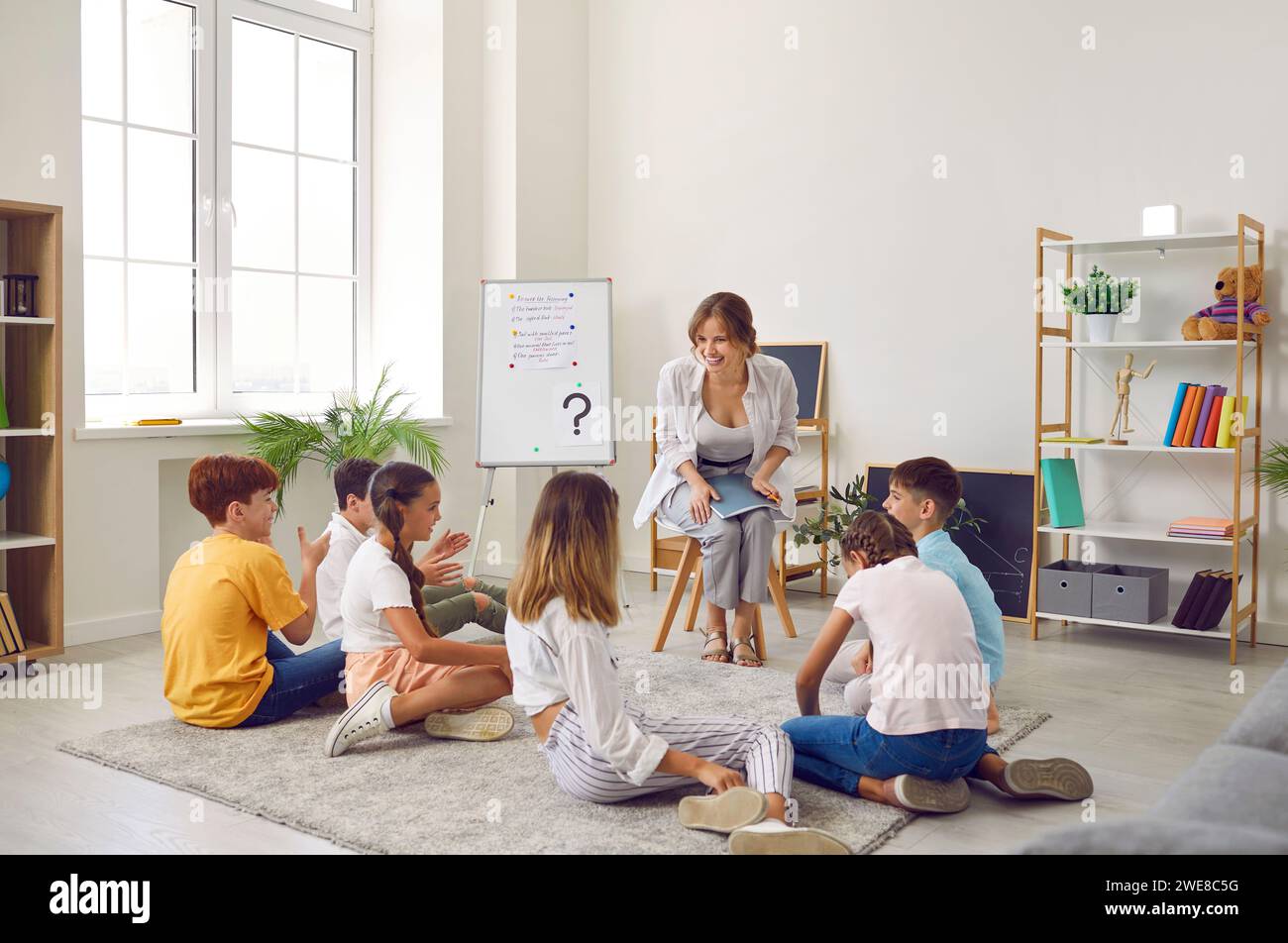 Groupe d'élèves de l'école primaire assis sur le sol écoutant l'enseignant en classe Banque D'Images