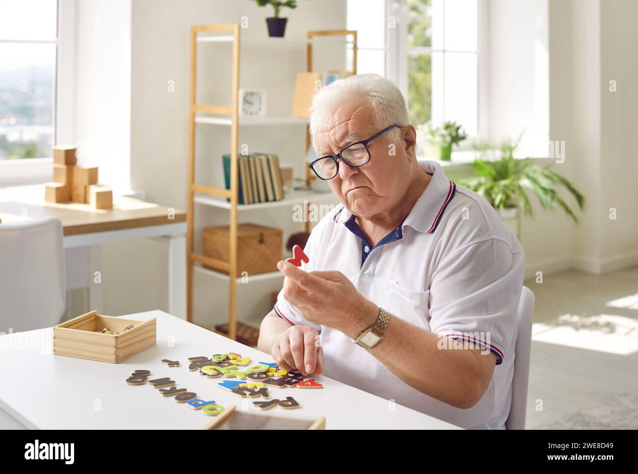 Homme âgé atteint de démence assis à table, jouant à des jeux et essayant de résoudre des énigmes Banque D'Images