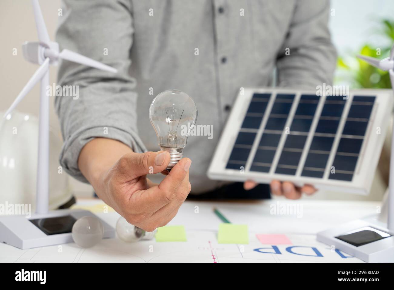 Homme d'affaires tenant des panneaux solaires et des ampoules au bureau. Banque D'Images