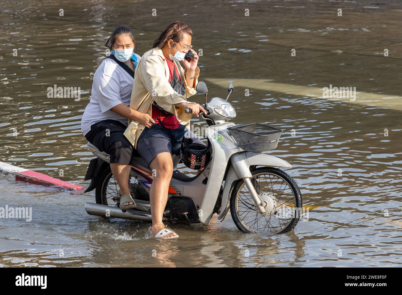 SAMUT PRAKAN, THAÏLANDE, NOVEMBRE 28 2023, deux femmes conduisent une moto dans une rue inondée Banque D'Images