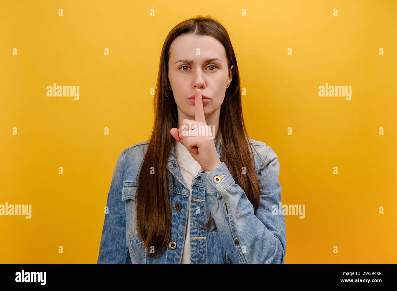 Portrait d'une jeune femme sérieuse montrant un geste de silence avec le doigt sur la bouche, demandant à rester silencieux, garder un concept secret, porter une veste en denim, poser Banque D'Images