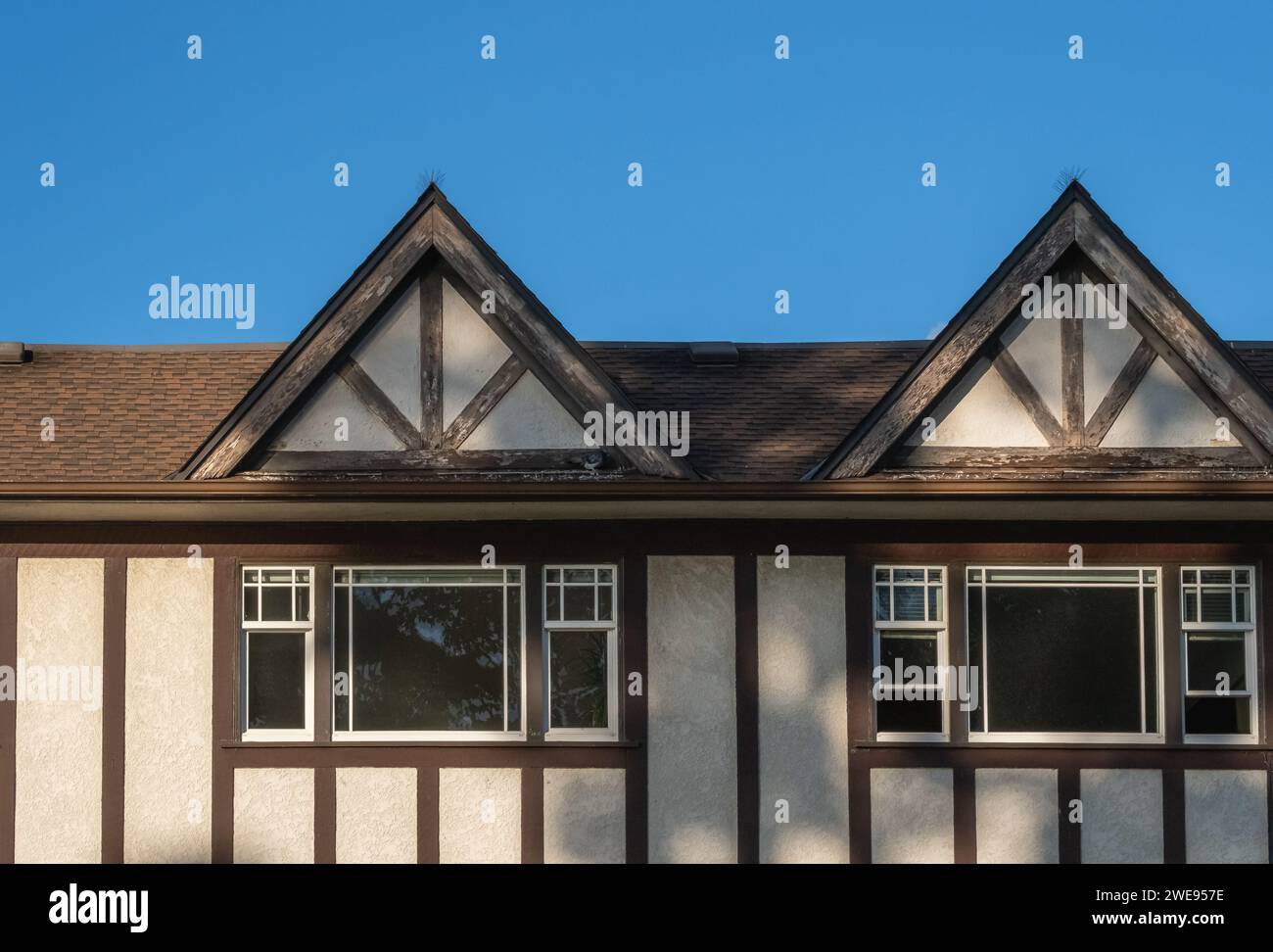 Le toit de la maison avec de belles fenêtres. Maisons avec toit en bardeaux contre ciel bleu. Bord des bardeaux de toit sur le dessus des maisons tuiles foncées d'asphalte sur t Banque D'Images