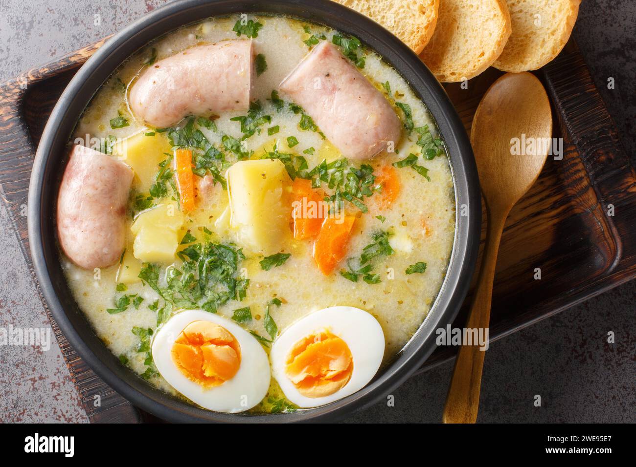 zurek polonais une soupe riche assaisonnée avec une entrée de seigle fermenté, servie avec un œuf bouilli coupé en deux et une saucisse blanche charnue en gros plan dans un bol sur la table. Banque D'Images