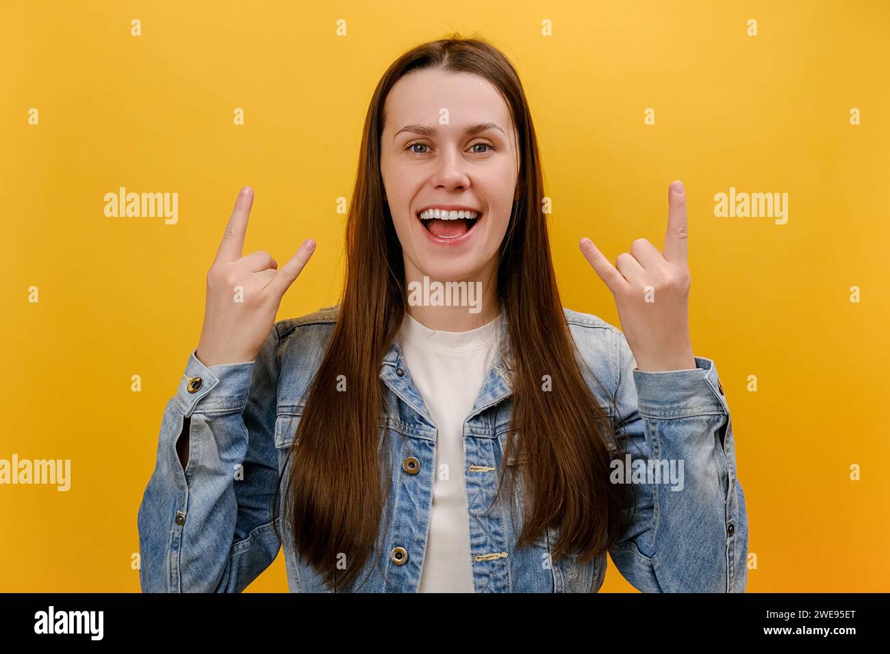 Portrait d'une jeune femme joyée montrant le signe de main rock and roll, criant et faisant des gestes au heavy Metal, musique rock, portant une veste en denim, posant est Banque D'Images