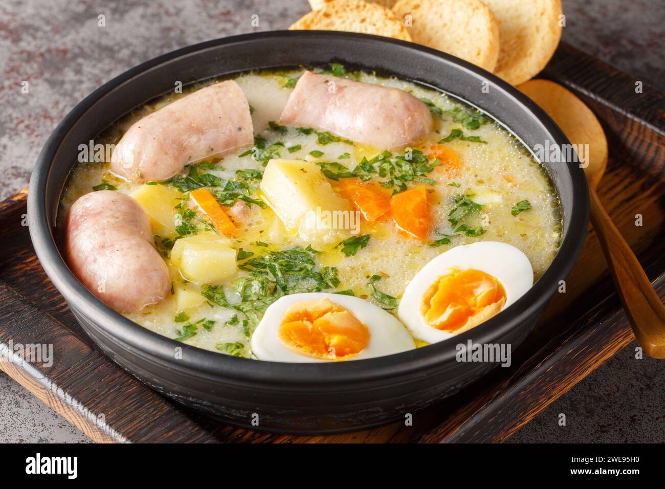 zurek polonais une soupe riche assaisonnée avec une entrée de seigle fermenté, servie avec un œuf bouilli coupé en deux et une saucisse blanche charnue en gros plan dans un bol sur la table. Banque D'Images