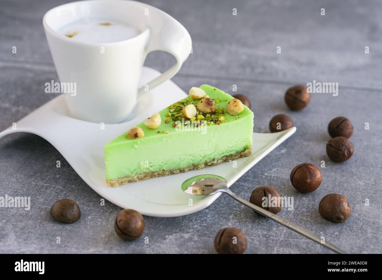 Gâteau au pistache vert avec noix de macadamia sur une assiette blanche et cappuccino. Cheesecake crémeux à la pistache Banque D'Images
