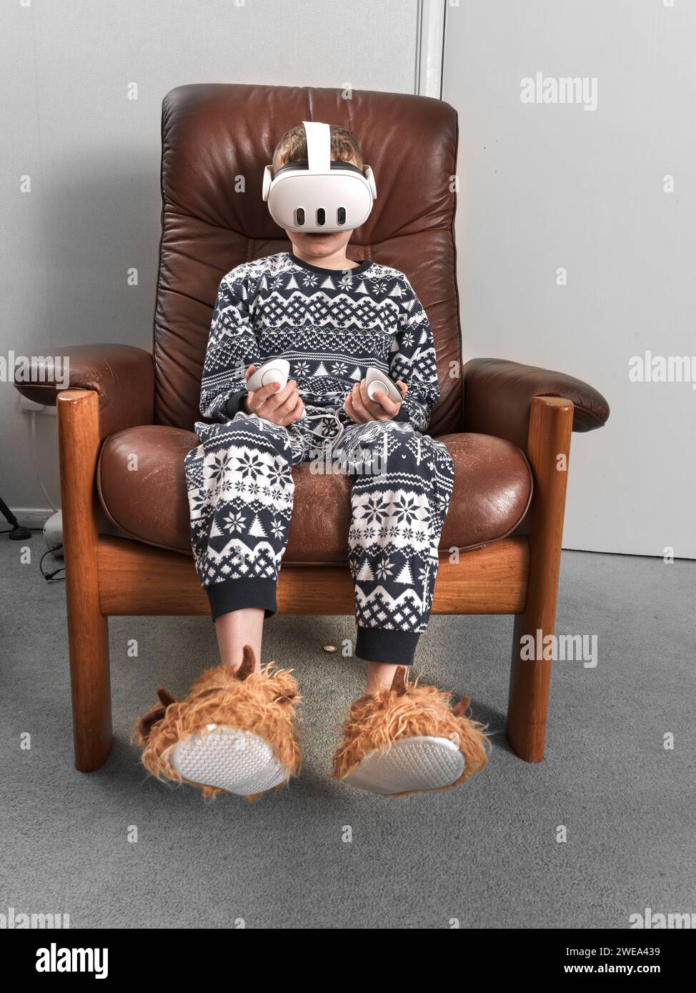Un ensemble de réalité virtuelle donné comme cadeau de chirstmas est utilisé par un jeune garçon assis sur une chaise. Banque D'Images