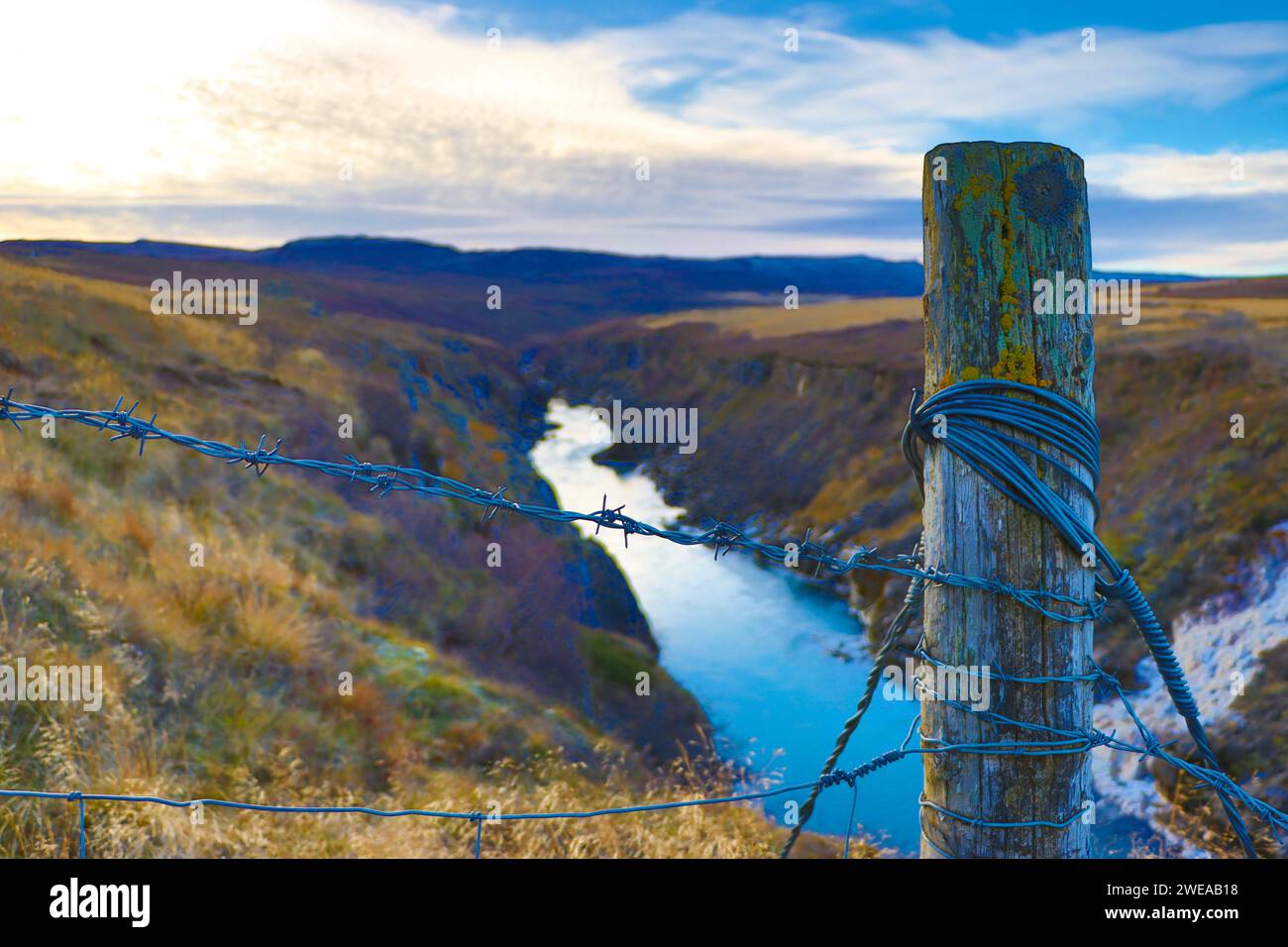 vue sur une rivière depuis une clôture en fil de fer barbelé et un tronc en bois rempli de lichens. Islande Banque D'Images