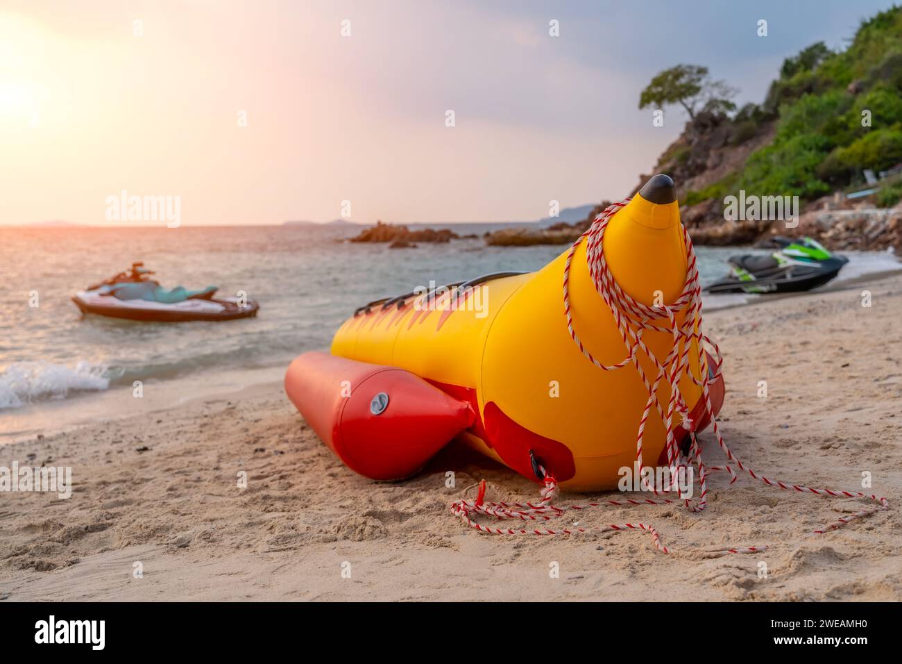 Banane gonflable pour les touristes d'équitation sur une plage tropicale pittoresque de sable pendant le coucher du soleil. Un scooter des mers dans l'eau en arrière-plan. Banque D'Images