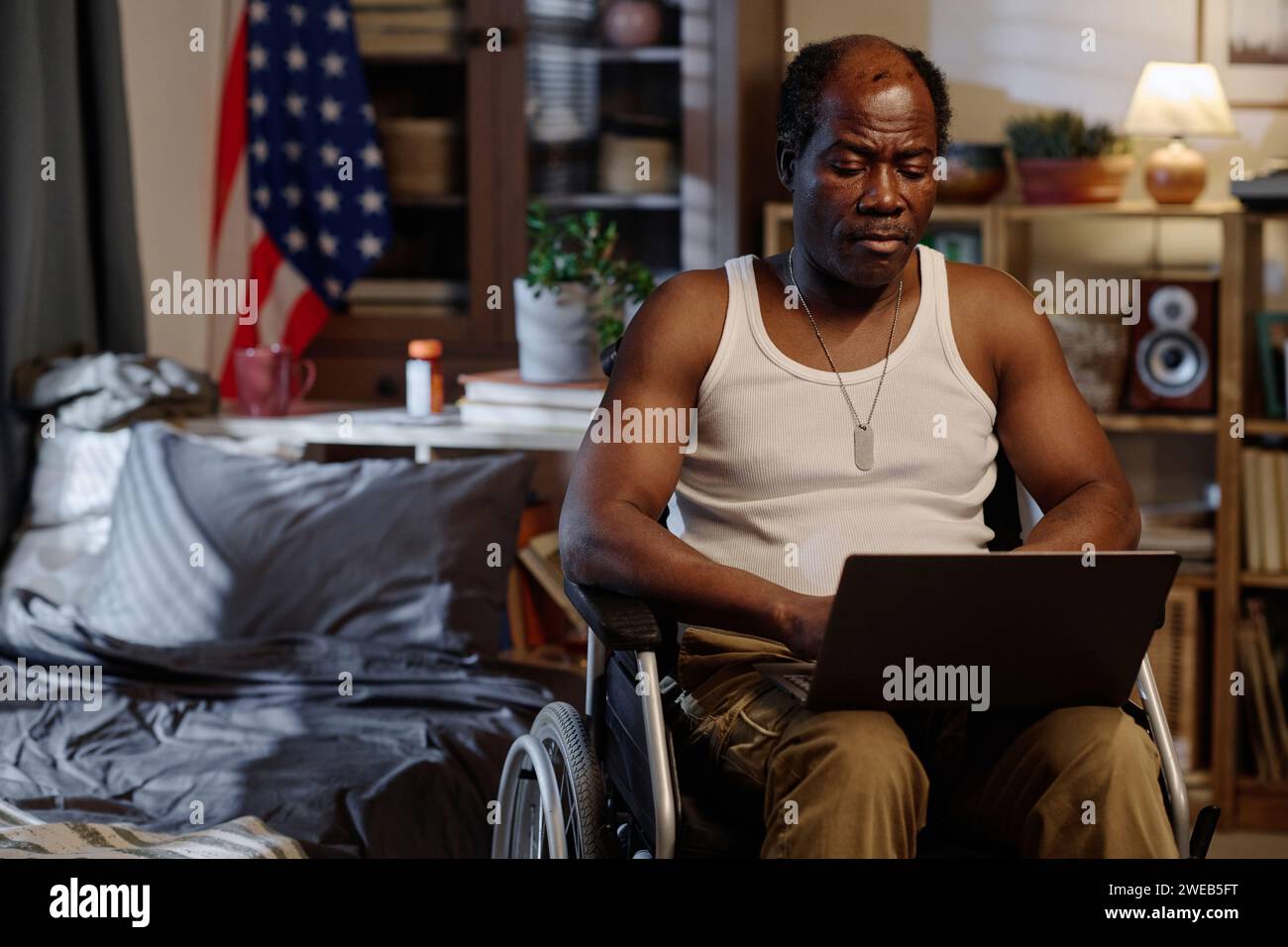 Homme afro-américain retraité avec un handicap physique travaillant de chez lui sur son ordinateur portable Banque D'Images