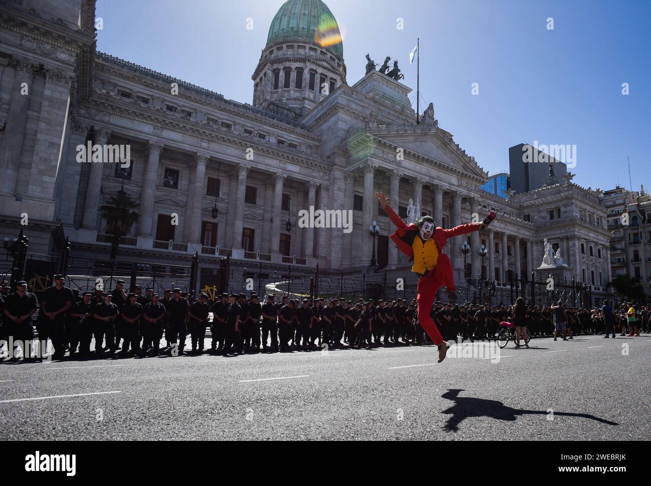 Buenos Aires, Argentine. 24 janvier 2024. Un homme habillé en joker saute devant une rangée de policiers devant le Congrès lors d'une manifestation contre le plan de réforme du gouvernement ultra-libéral du président Milei le jour d'une grève générale. Les syndicats ont appelé à la grève générale. Avec une inflation de 211,4%, le nouveau gouvernement veut faire adopter un programme radical d’austérité et de réforme. Crédit : Martin Cossarini/dpa - ATTENTION : à usage éditorial uniquement et uniquement avec référence complète au crédit/dpa/Alamy Live News ci-dessus Banque D'Images