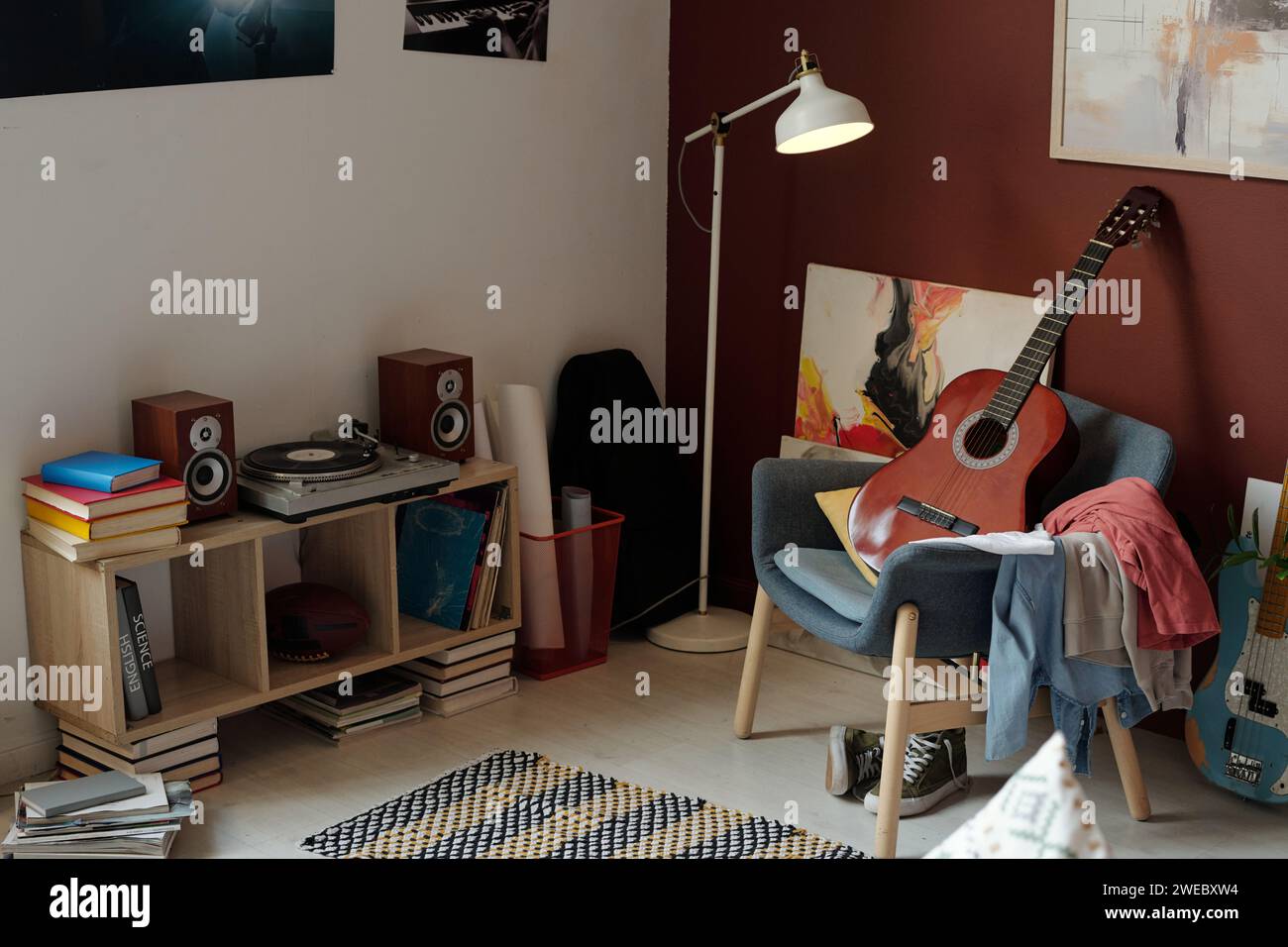 Nouvelle guitare acoustique debout sur fauteuil avec pile de vêtements devant le tourne-disque entouré de livres et de deux haut-parleurs sonores Banque D'Images